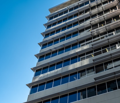 A modern, multi-story office building with rows of large, reflective glass windows and a sleek, geometric design set against a clear blue sky.