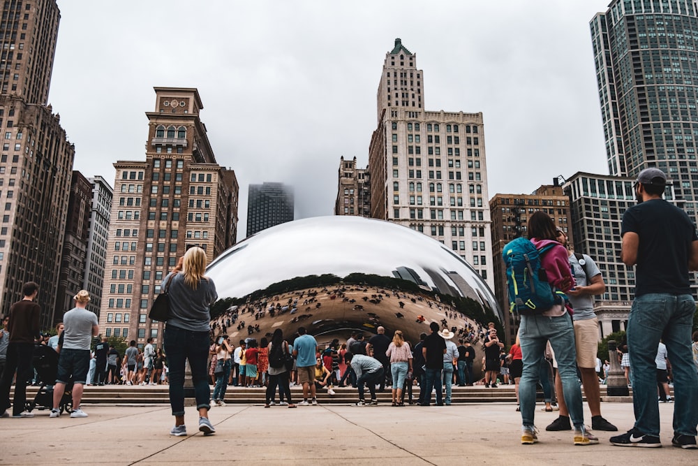 a group of people standing around a reflective sphere in a city