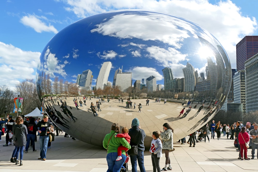 a large reflective sphere with people around it with Millennium Park in the background