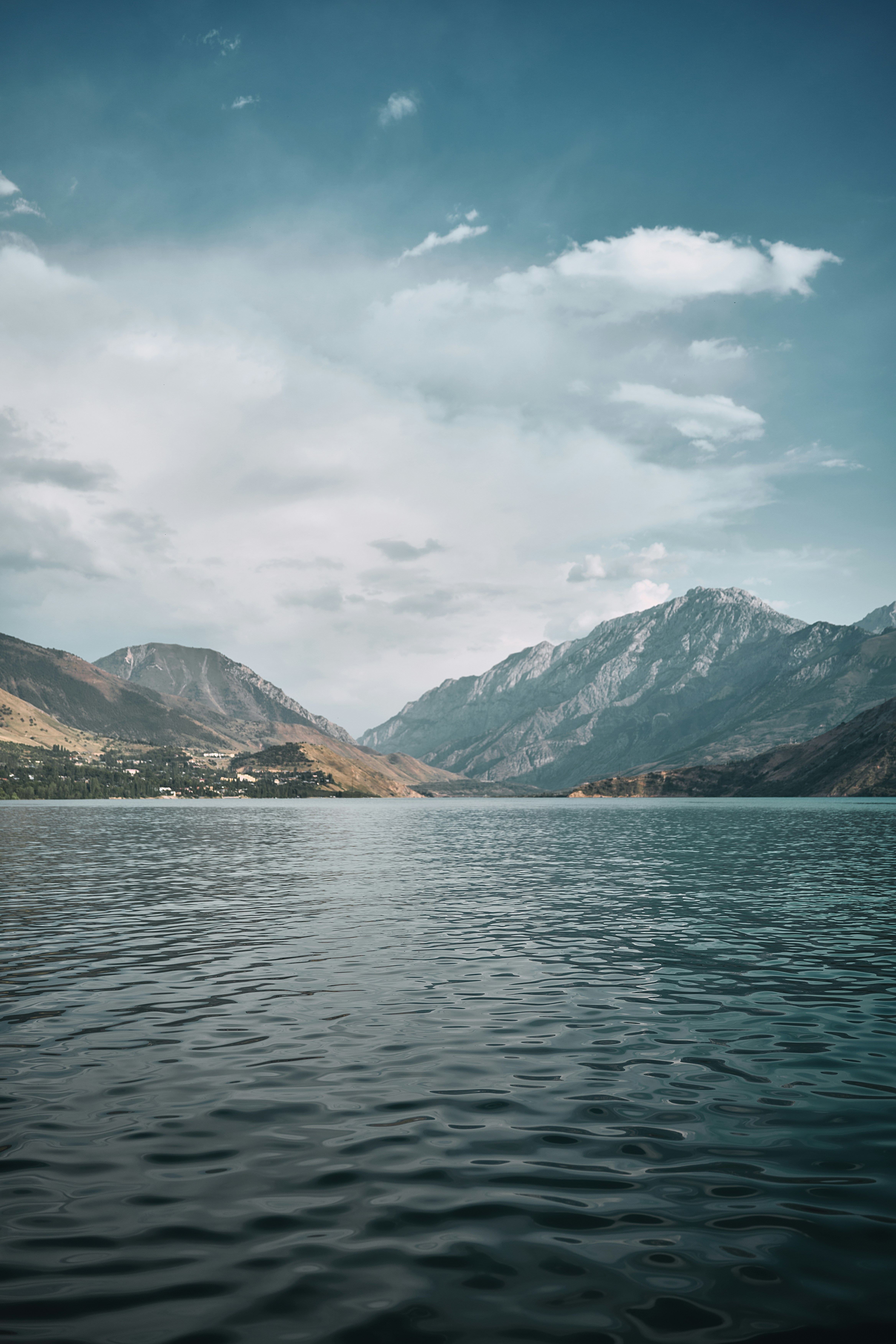 Glassy alpine lake with rugged mountain peaks along the horizon under a pale blue sky.