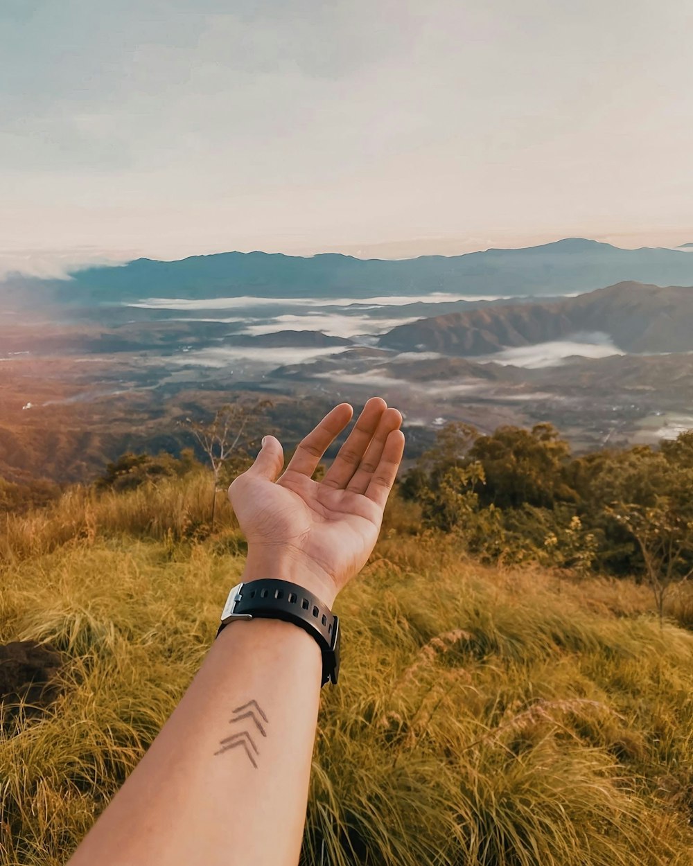 uma mão com um relógio em uma colina com vista para um vale