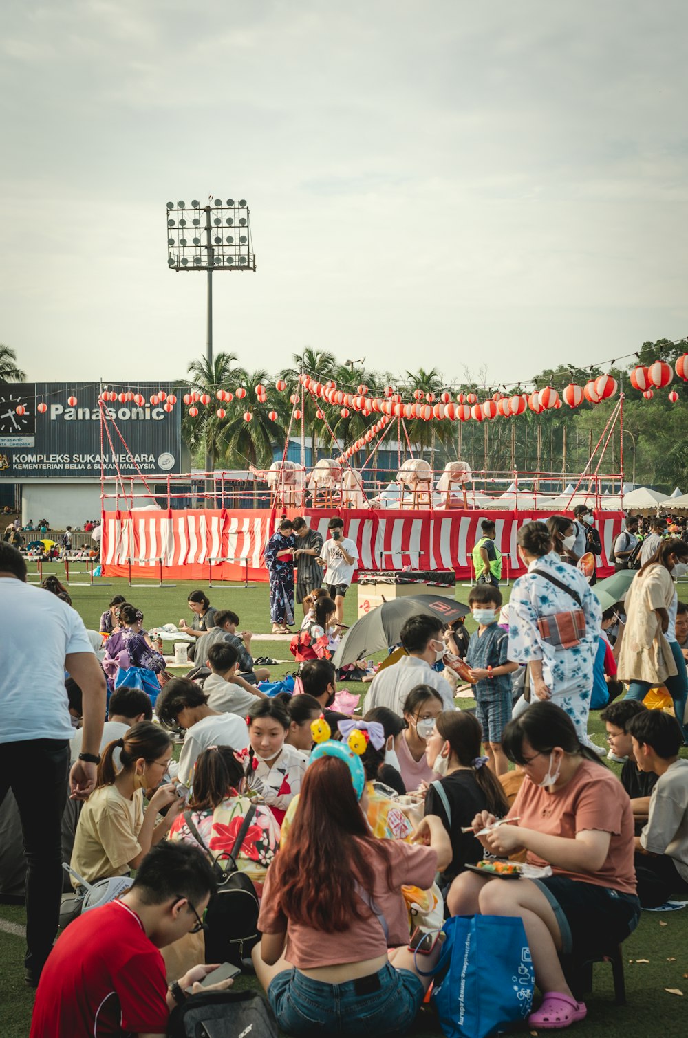 a crowd of people sitting on the ground with a stage in the back