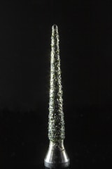 A metallic, conical object stands vertically against a dark background. Its surface is textured with a rough, clustered pattern that reflects light, creating a sparkling effect.