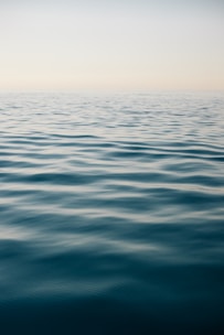 An impressionistic watercolor of a calm sea under a pale blue sky, with subtle reflections on the water.