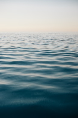 An impressionistic watercolor of a calm sea under a pale blue sky, with subtle reflections on the water.