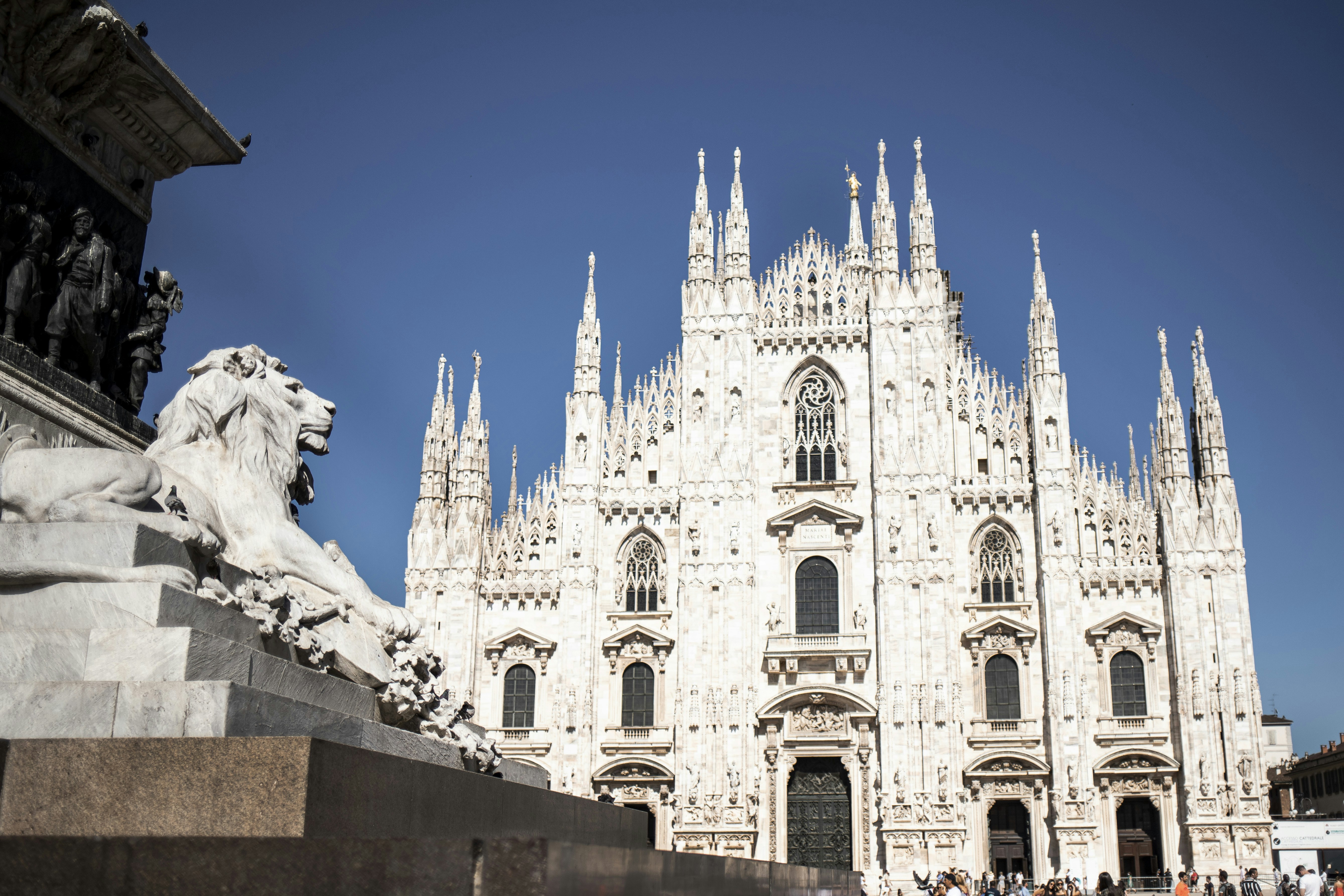 A large white building with a statue in front of it with Milan Cathedral in the background