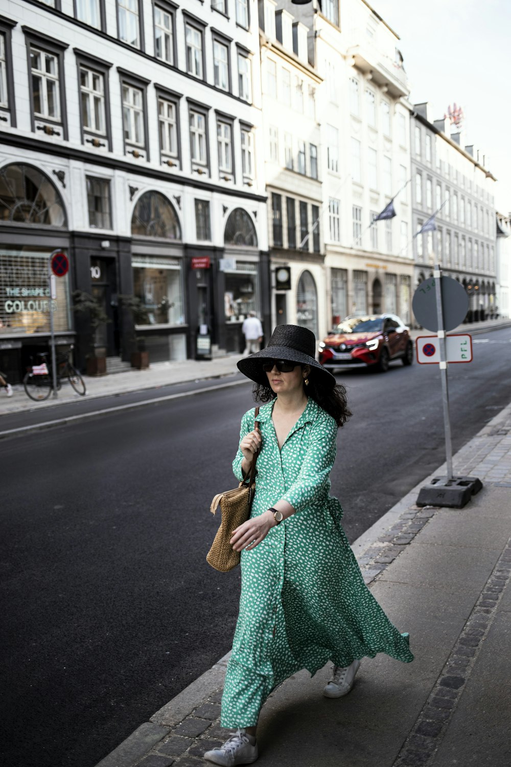 a woman in a green dress and hat walking down a street