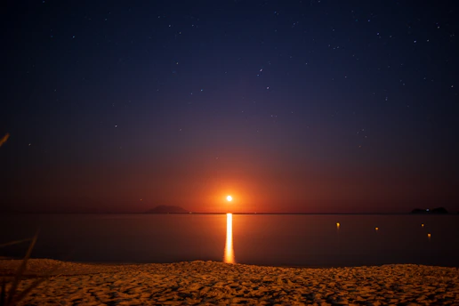 A serene nighttime beach scene lit by glowing Japanese lanterns and tiki torches, evoking a mystical atmosphere.