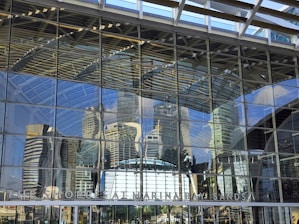 Modern glass facade of a London commercial building reflecting the city skyline on a clear day.