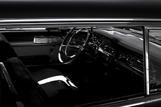 A vintage car interior showcasing a classic steering wheel, sleek dashboard with chrome detailing, and plush seating. The image captures a sense of nostalgia and elegance.