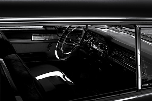A vintage car interior showcasing a classic steering wheel, sleek dashboard with chrome detailing, and plush seating. The image captures a sense of nostalgia and elegance.
