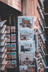 A display of calendars and postcards featuring images of Rome, including pictures of famous landmarks like the Colosseum and cats. The setup appears to be in a shop, with various calendar designs showing Roman architecture and feline imagery.