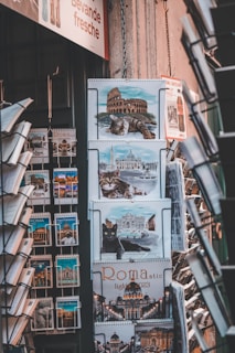 A display of calendars and postcards featuring images of Rome, including pictures of famous landmarks like the Colosseum and cats. The setup appears to be in a shop, with various calendar designs showing Roman architecture and feline imagery.
