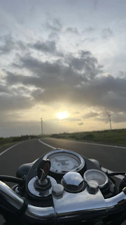 A close-up of a motorcycle dashboard with a scenic road ahead at sunset.