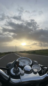 A close-up of a motorcycle dashboard with a scenic road ahead at sunset.