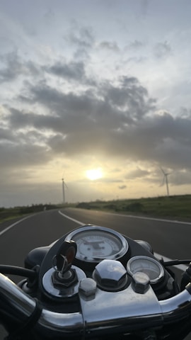 A close-up of a motorcycle dashboard with a scenic coastal road ahead at sunset.