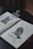 An open sketchbook rests on a dark surface, displaying detailed illustrations of a rabbit on the left page and an owl perched on a branch on the right page. The sketchbook is held open by a large metallic clip. Small color swatches are visible beneath each illustration, suggesting a focus on texture and detail.