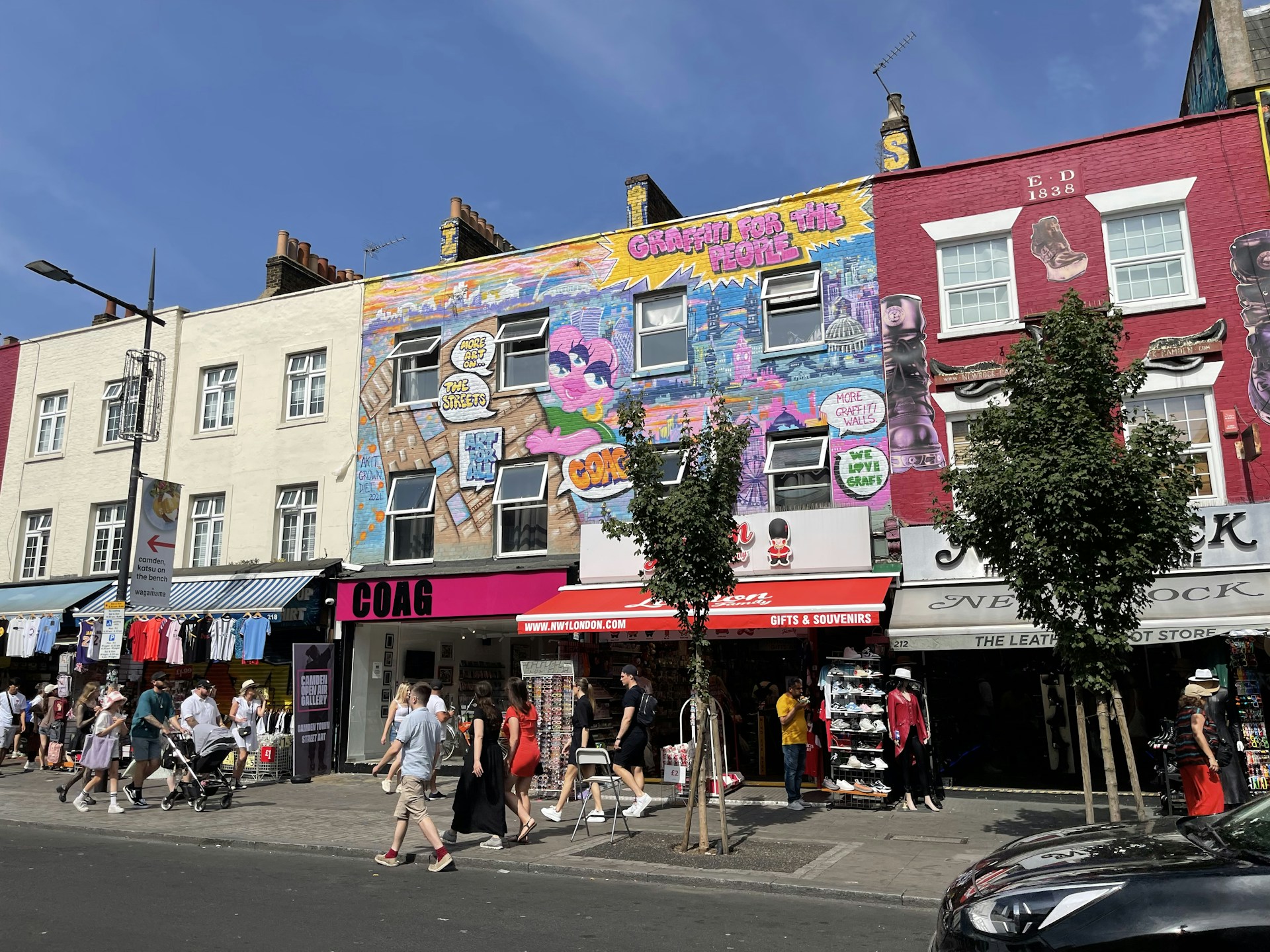 An urban street scene with lively crowds and striking street art murals on the buildings.