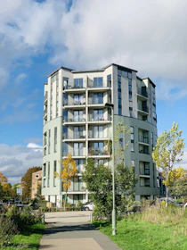 A modern residential building surrounded by green spaces under a clear sky.