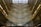 An architectural interior with multiple levels featuring ornate patterns on the walls and a large glass roof allowing natural light to flood in. The design creates an intricate and mesmerizing visual effect with a complex mosaic of light and shadow.