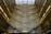 An architectural interior with multiple levels featuring ornate patterns on the walls and a large glass roof allowing natural light to flood in. The design creates an intricate and mesmerizing visual effect with a complex mosaic of light and shadow.