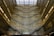An architectural interior with multiple levels featuring ornate patterns on the walls and a large glass roof allowing natural light to flood in. The design creates an intricate and mesmerizing visual effect with a complex mosaic of light and shadow.