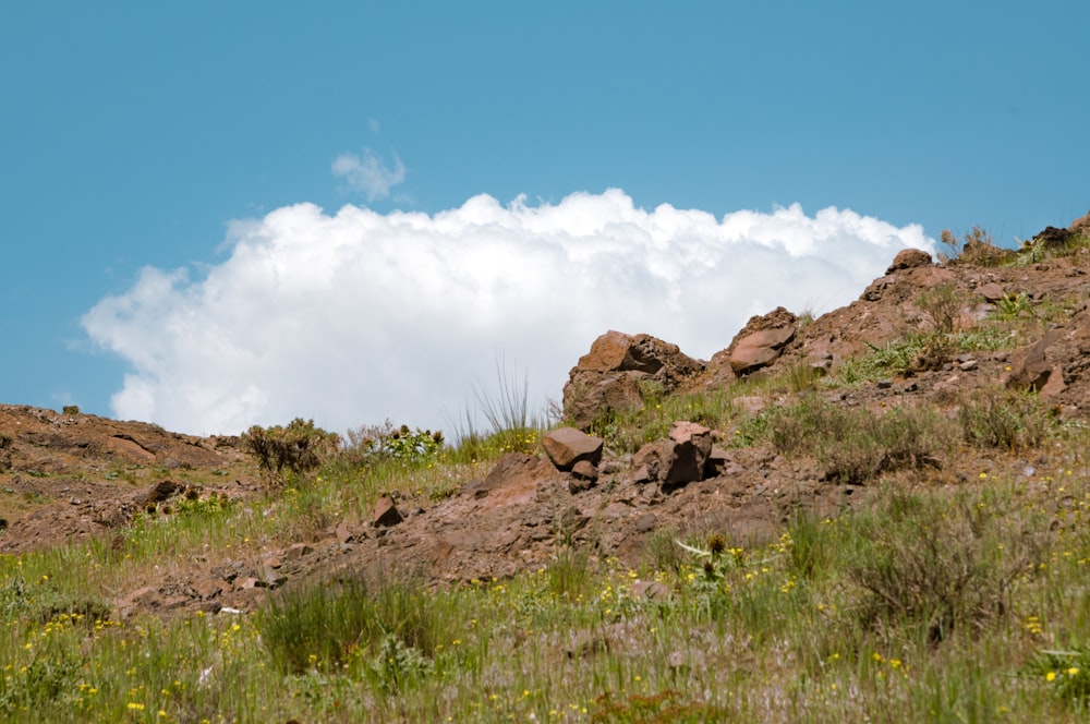 a rocky hill with grass and a cloudy sky