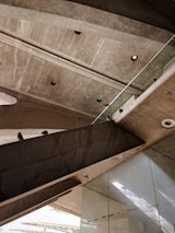 A photograph showcasing an architectural concrete structure with multiple levels and sharp angles. The ceiling has several recessed circular lights, and there are two pigeons perched on the concrete ledges. Glass panels and reflective surfaces are visible in the lower part of the image.