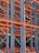 A complex structure composed of multiple metal beams and girders, mainly in dark blue and orange hues. The intricate, crisscrossing framework suggests the interior of an industrial racking system, possibly used for storage or support.