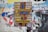A vibrant poster with bold, colorful text and a zigzag lightning bolt design is pasted onto a textured brick wall. The surrounding area is layered with torn scraps of other posters and paper, creating a collage effect.
