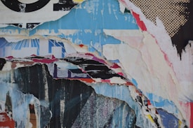 Various layers of torn paper revealing snippets of text and design from older posters, creating a collage effect with rough edges and overlaps. The composition is abstract, featuring patterns like dots and fragments of text.