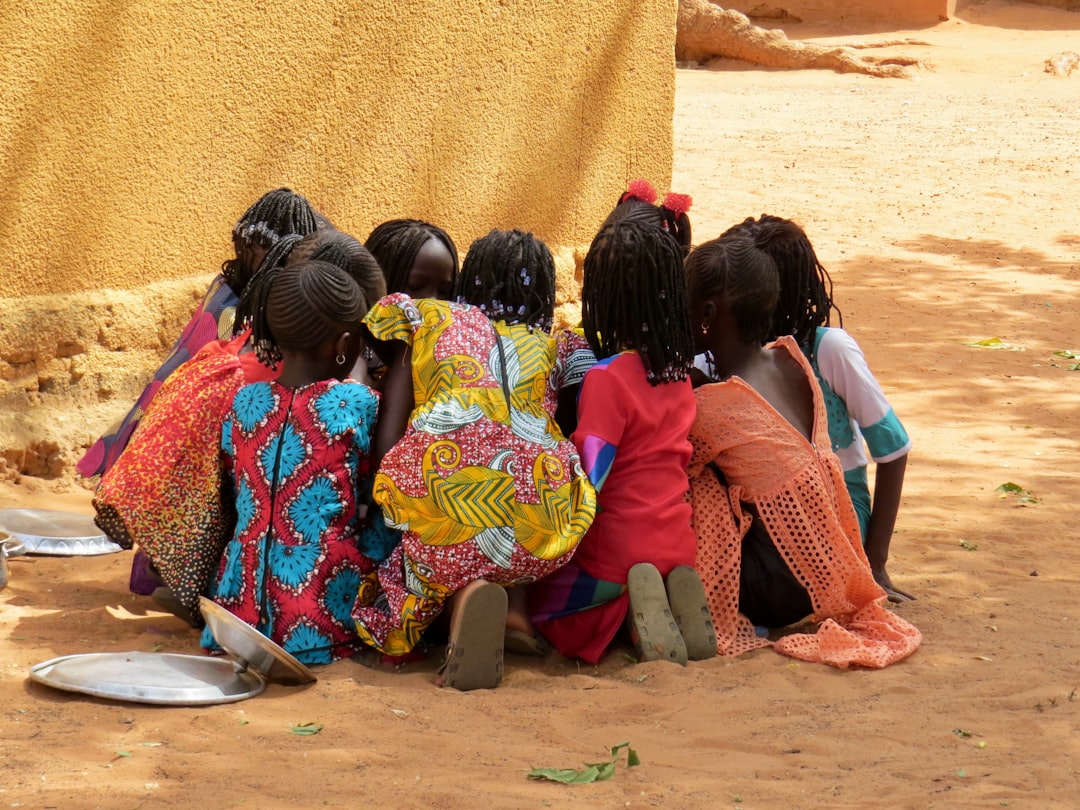 a group of children sitting on the ground, Eating together from one bowl