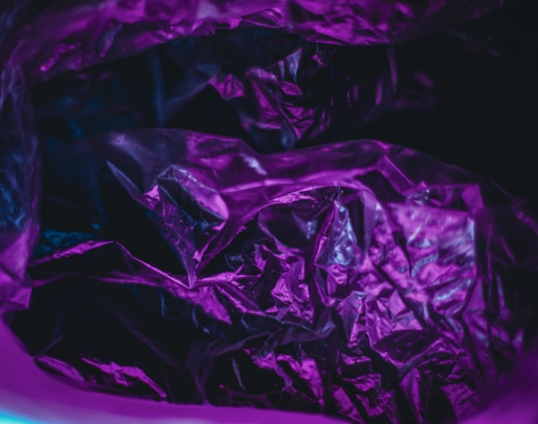Wrinkled purple plastic material with glossy texture, highlighted by a mix of pink and blue hues in moody lighting.