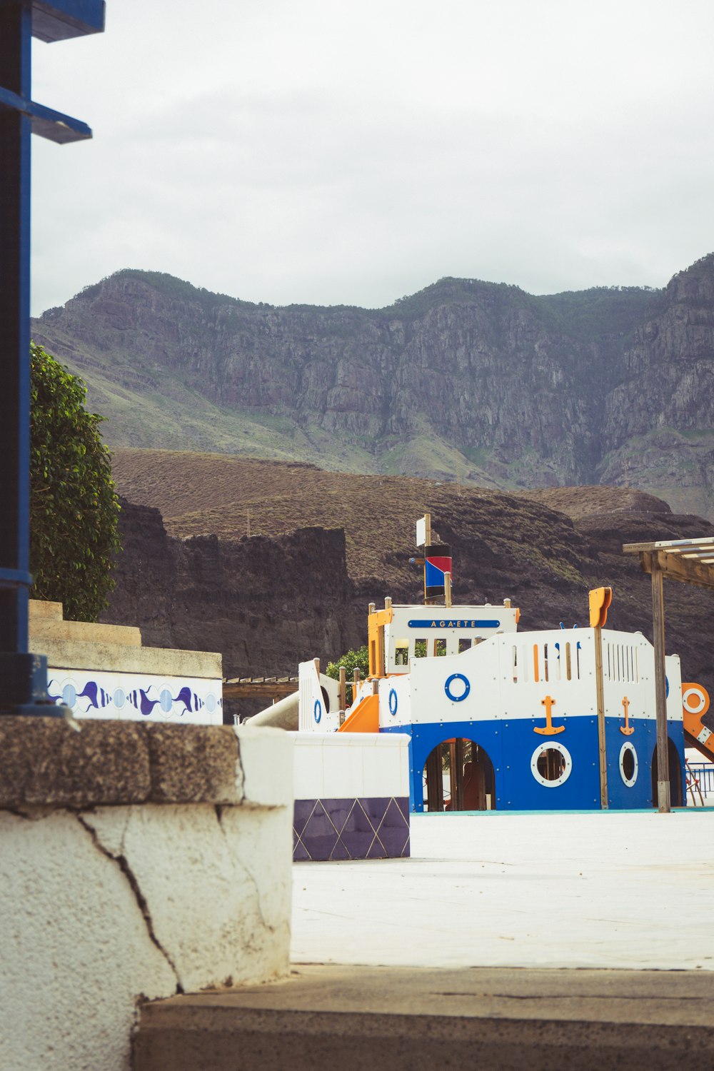 a blue and white boat on a stone wall with mountains in the background