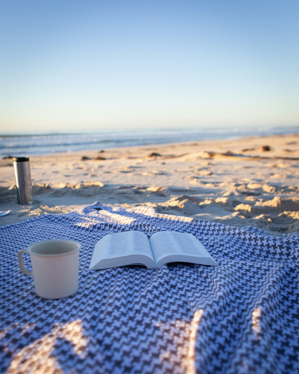 a book and a cup on a beach