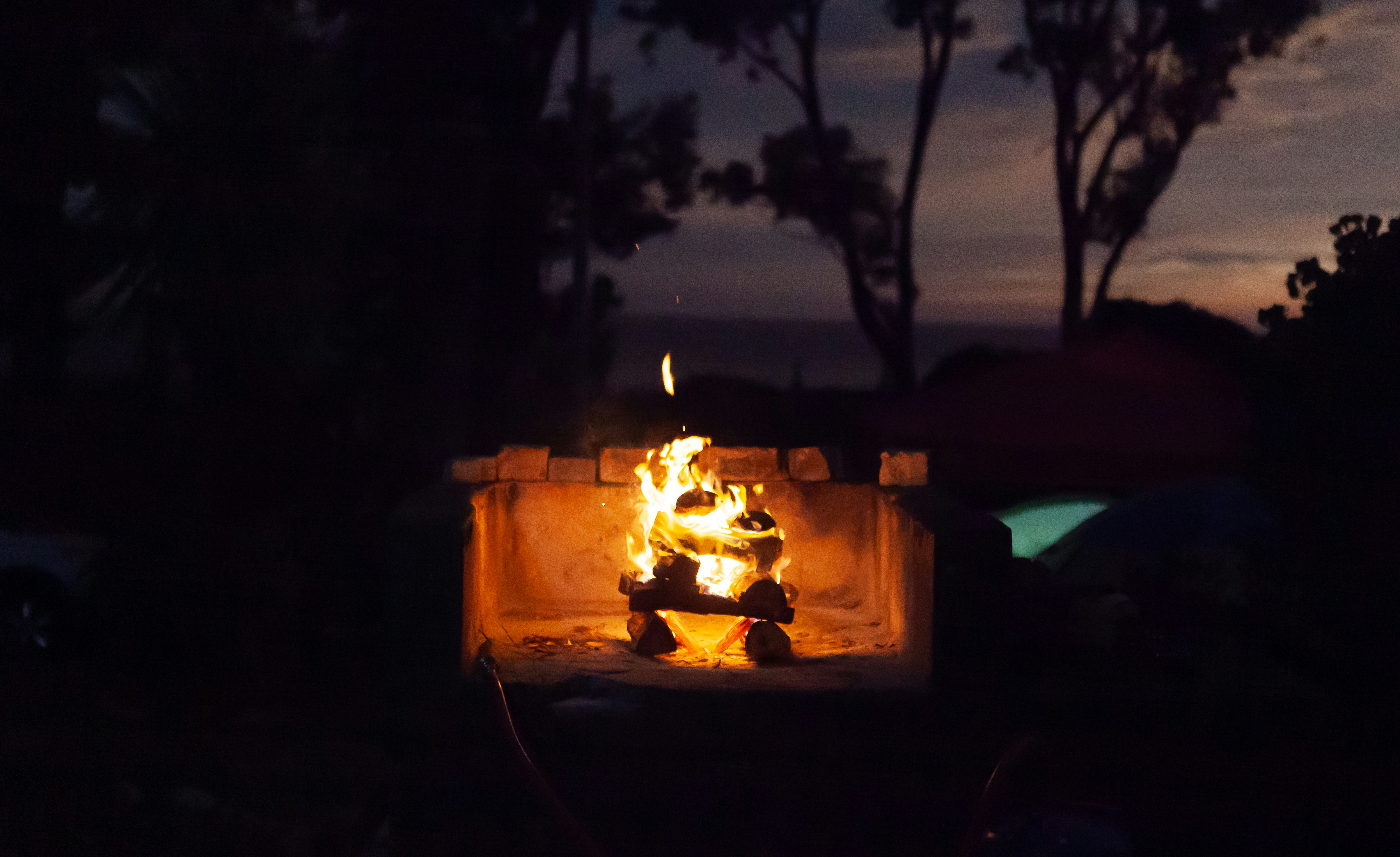 Evening braai fire glowing in a stone pit, dark atmospheric surroundings, warm ember light, communal gathering space