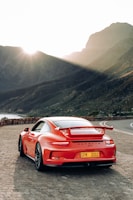 A sleek red sports car parked on a mountain road at sunset.