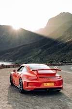 A sleek sports car parked on a scenic mountain road at sunset, highlighting its curves and design.