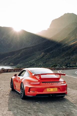 A sleek red sports car captured at sunset on a winding mountain road.