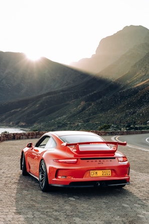 A sleek red sports car parked on a mountain road at sunset.