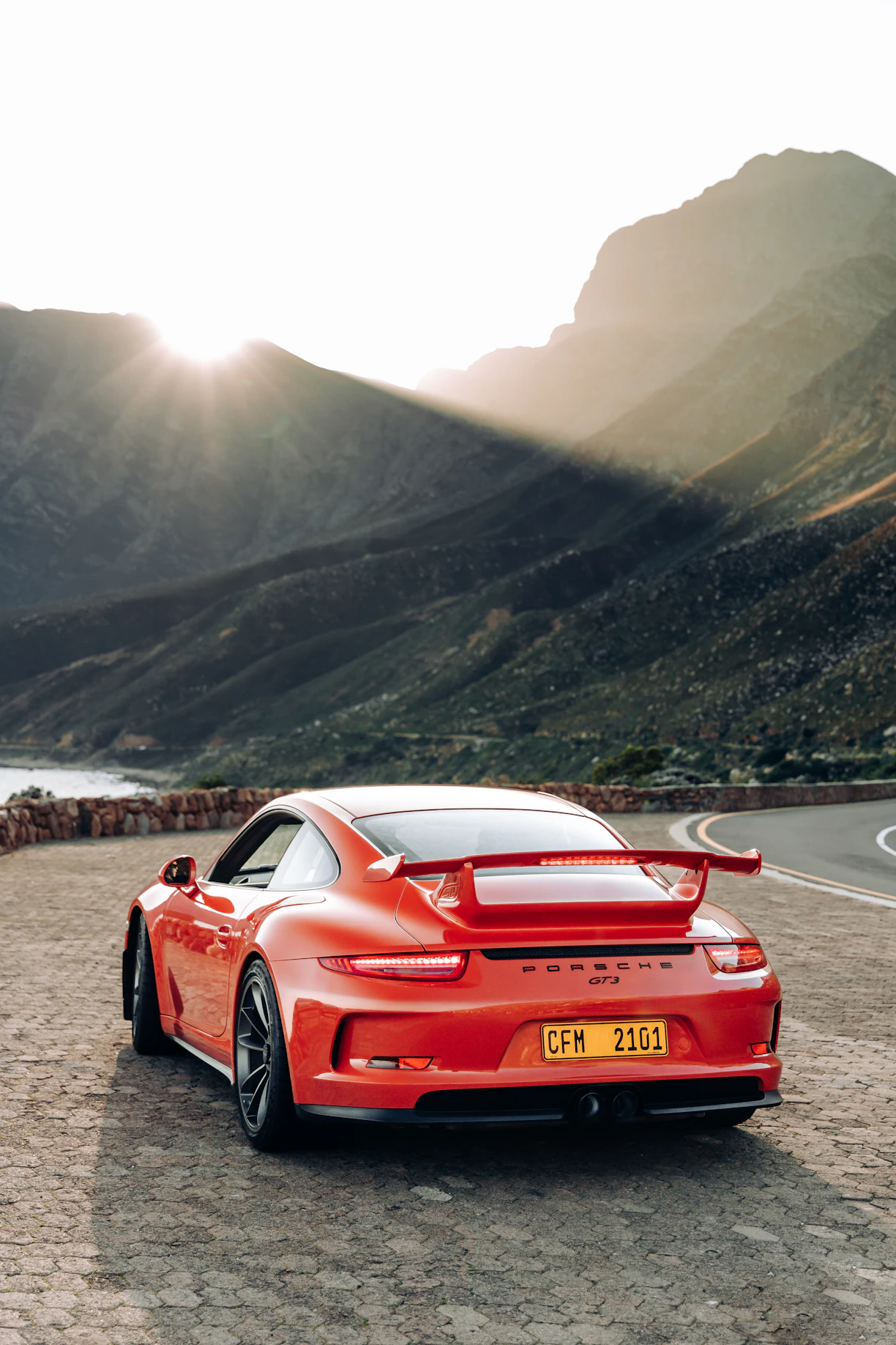 A sleek sports car parked on a scenic mountain road at sunset, highlighting its curves and design.