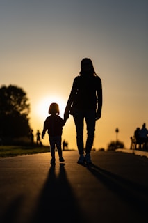 a woman and a child walking on a road with the sun setting