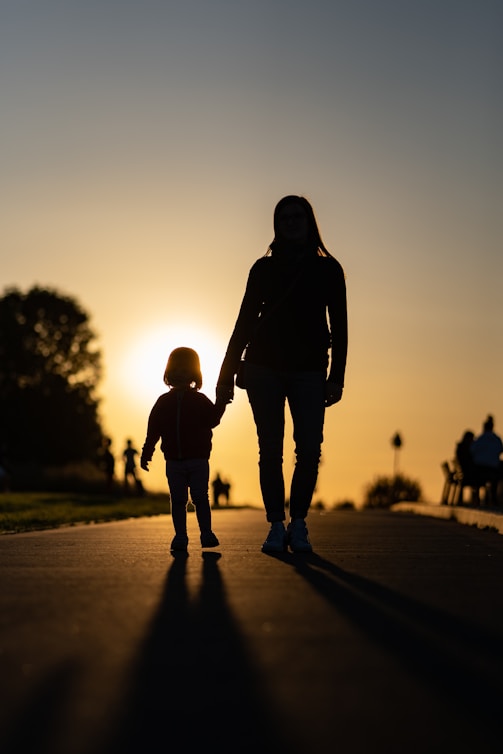 a woman and a child walking on a road with the sun setting