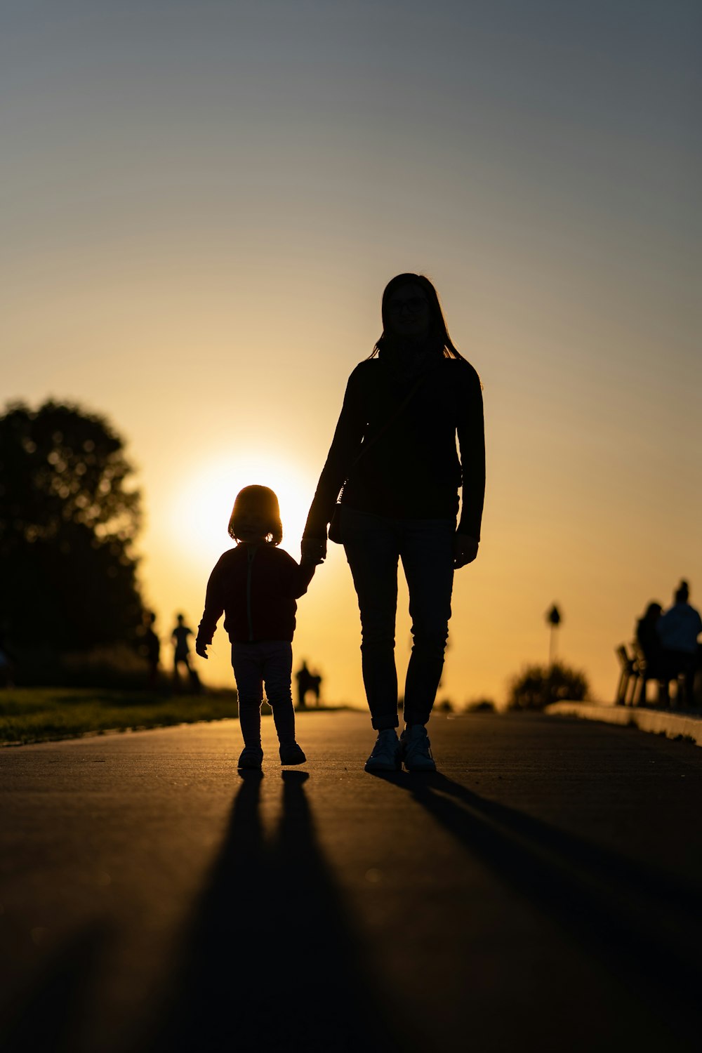 a man and a child walking on a road with the sun setting