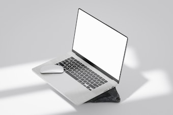 A laptop with a blank white screen is placed at an angle on a dark rock in a minimalist setting. Beside the laptop is a wireless mouse. The background is a light gray with soft shadows, creating a clean and modern aesthetic.