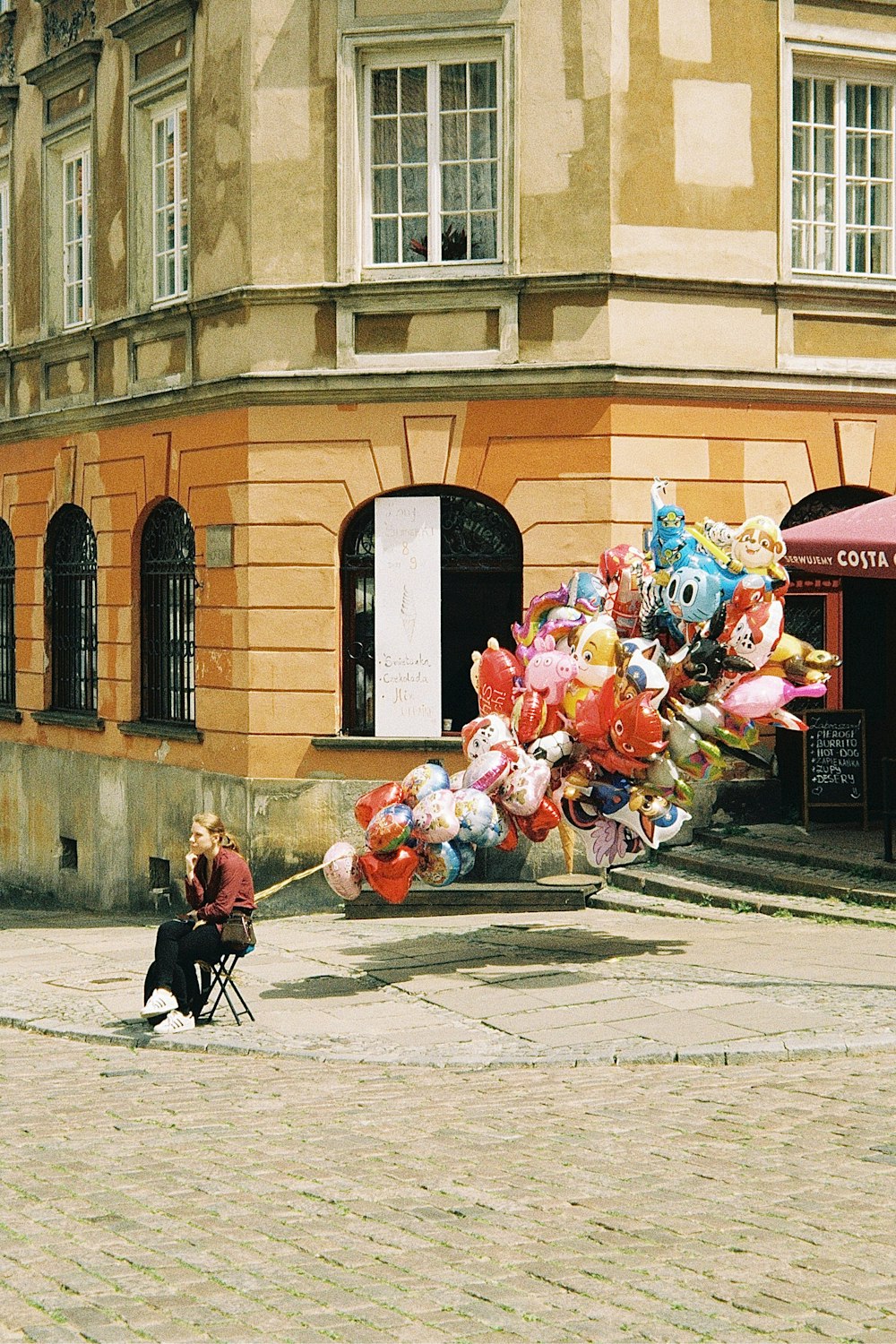 a person sitting on a sidewalk with a dog and a large pile of balloons