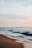Gentle waves lapping on a sandy shore under a pastel sky at dawn.