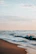 Gentle waves lapping on a sandy shore under a pastel sky at dawn.