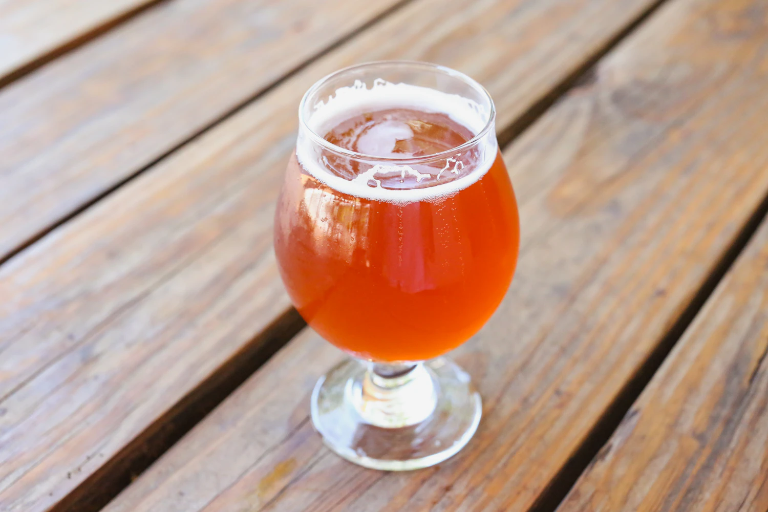 A copper-red amber ale in a round goblet on a weathered wooden table