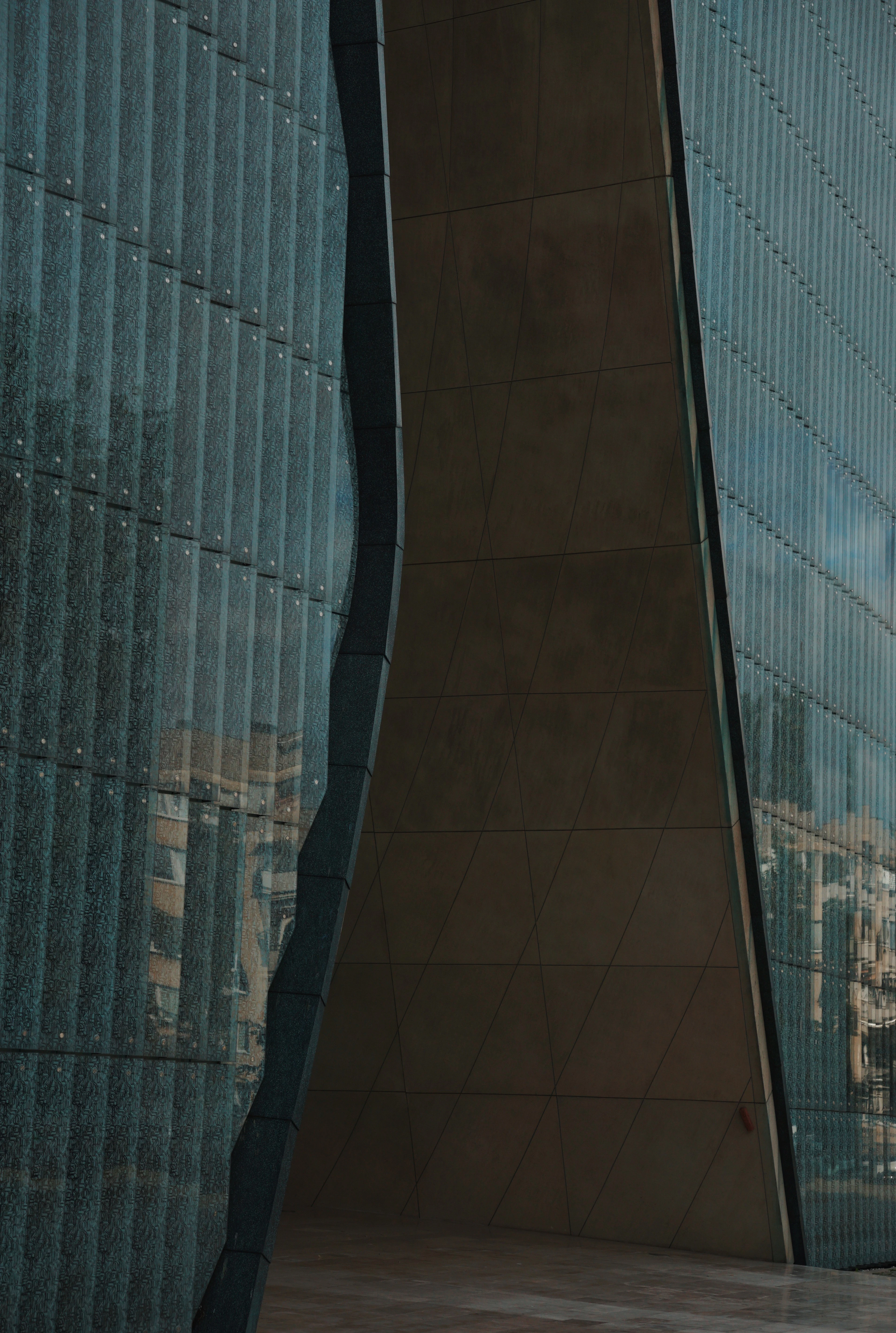 A modern museum's undulating glass and copper facade is split by a narrow crevice-like passage.